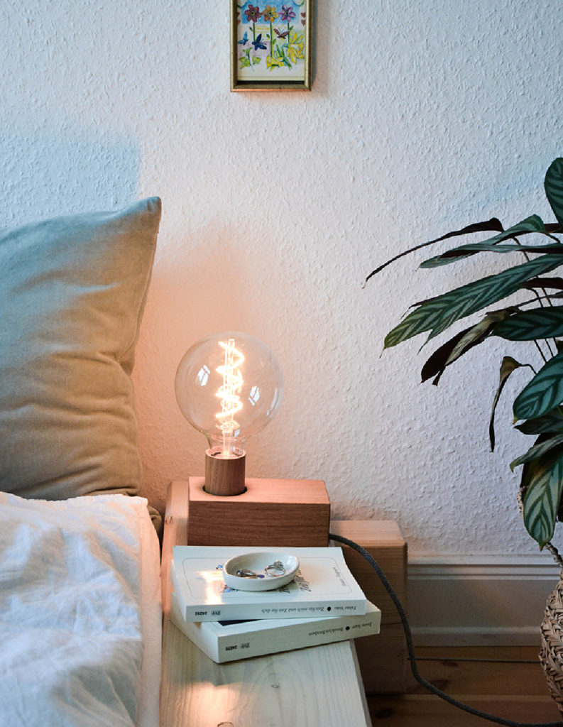Minimalistische Nachttischgestaltung mit Holz-Tischleuchte, Büchern und grüner Pflanze