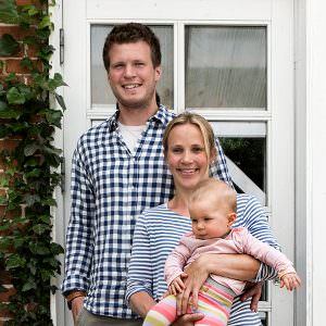 Zwei Menschen vor Fenster, halten Baby, komfortable Räumlichheit