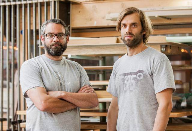 Zwei Männer in Grayshirts in einem Workraum mit Holzplanken und Werkzeugen
