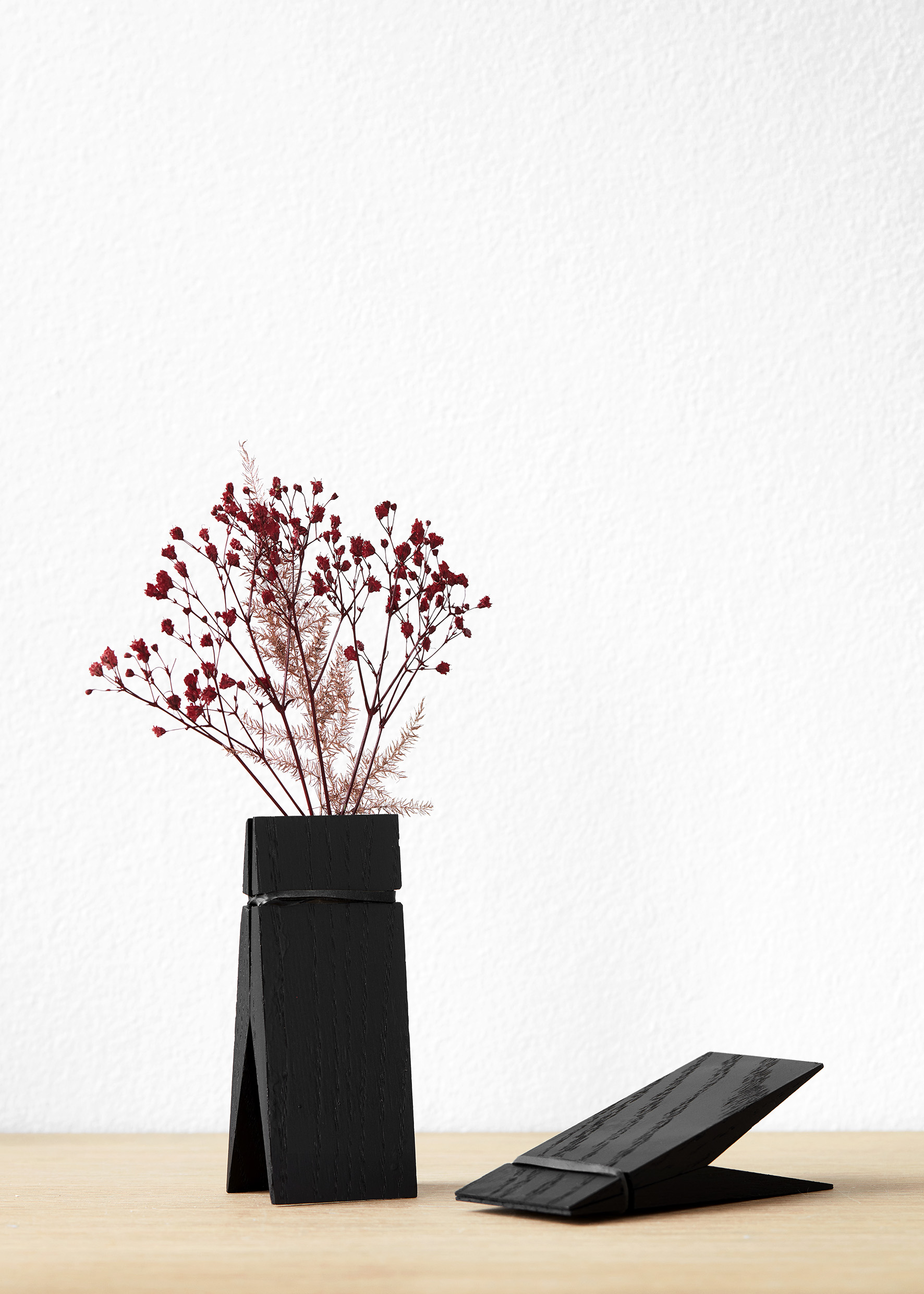 Trapezförmige schwarze Holzvase mit getrockneten Blüten auf hellen Holztisch