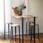 Holztisch mit Tiptoe-Beschlägen und schwarzen Barhockern in modernem Wohnambiente