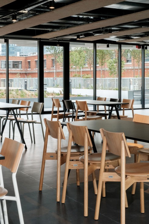 Elegante Designmöbel im hellen Showroom mit Holzstühlen, schwarzen Tischen und großflächigen Fenstern für modernes Interior