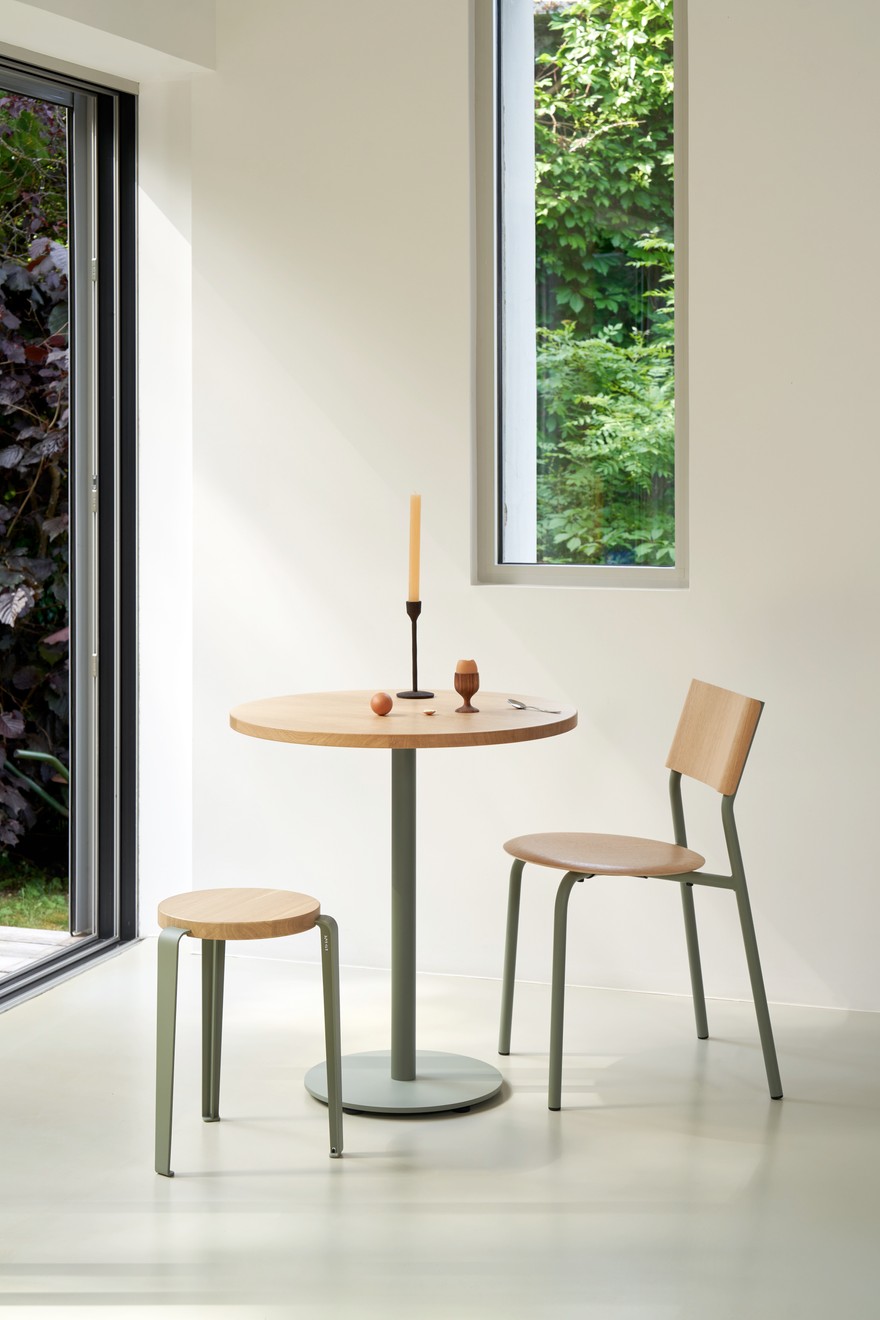 Minimalistische Essgruppe mit rundem Eichentisch, graugrünem Metallgestell, Holzstühlen und Hocker im hellen Interior