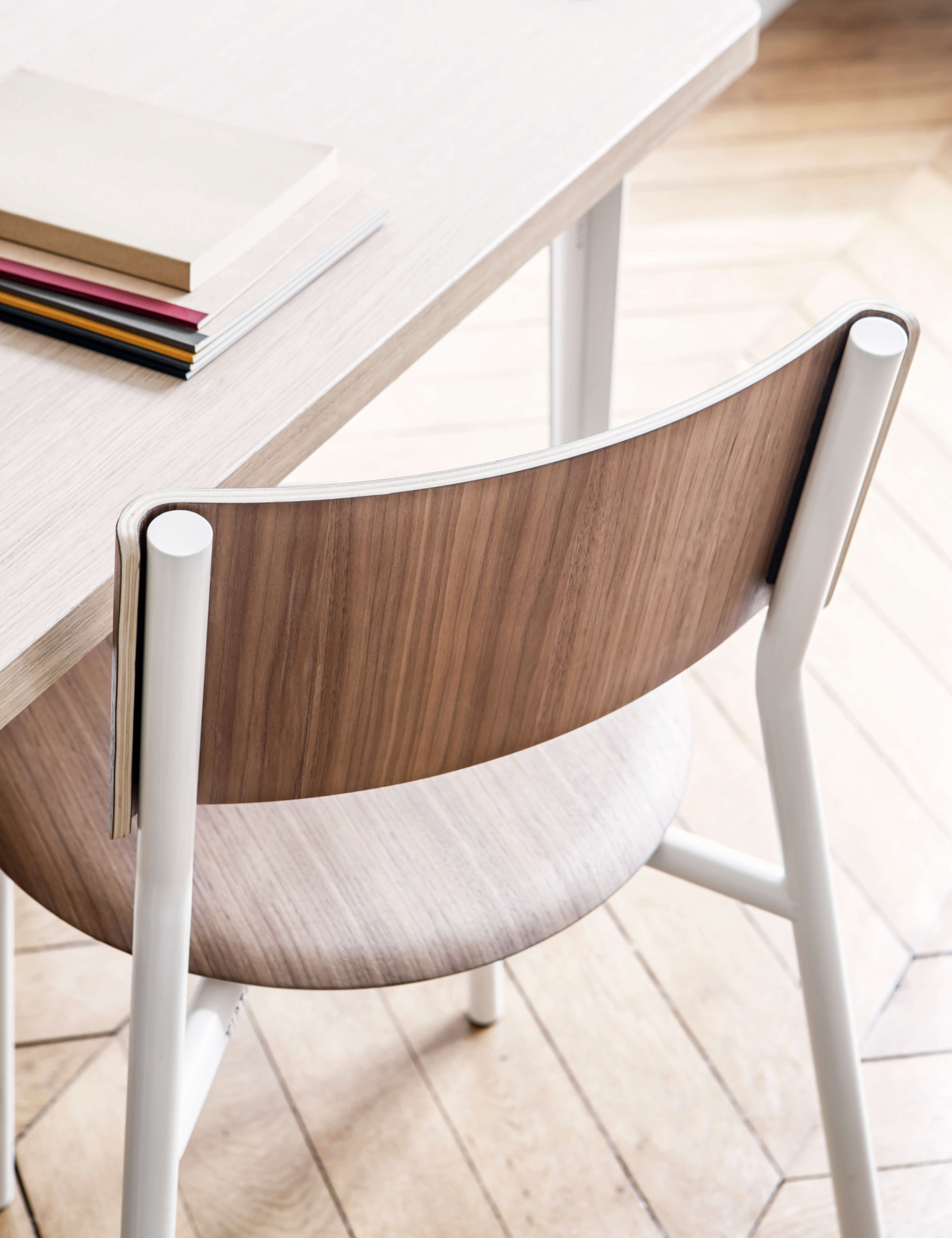 Moderner Designstuhl mit weißem Metallgestell und walnussholziger Rückenlehne auf minimalistischem Holztisch