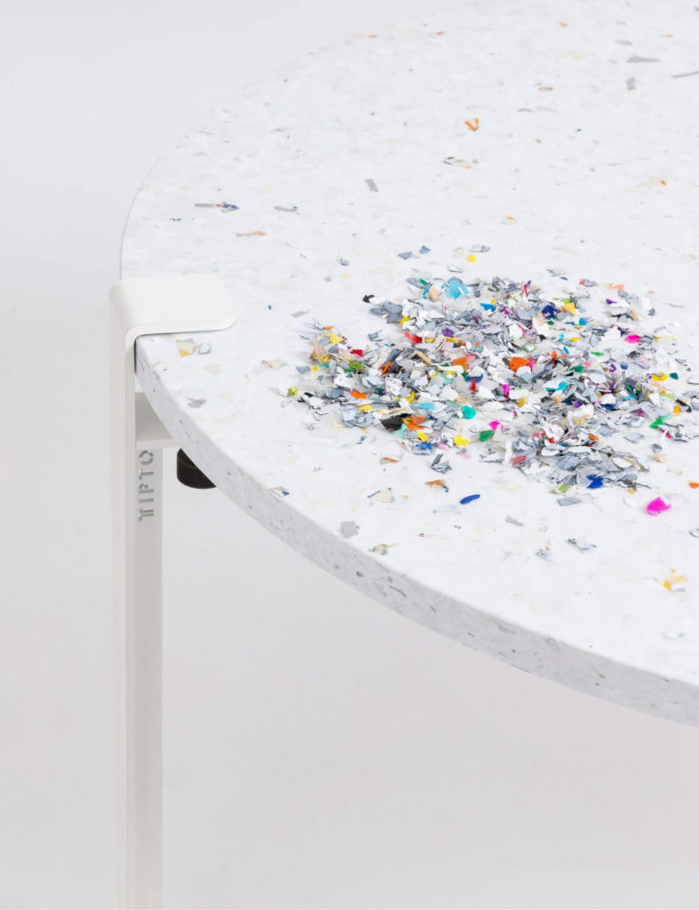 Weißer runder Tisch mit zerkleinerten Kunststoffteilen als nachhaltige Künstlerinstallation