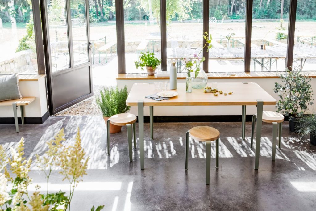 Minimalistisches Esszimmer mit Holztisch, graugrünen Beinen und grüner Vegetation