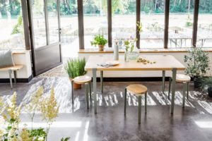 Minimalistisches Esszimmer mit Holztisch, graugrünen Beinen und grüner Vegetation
