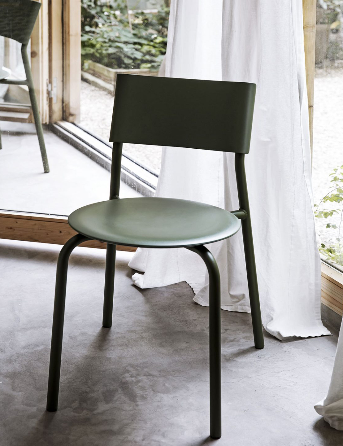 Moderner olivgrüner Designstuhl mit minimalistischen Linien in hellem Innenraum mit Gartenblick
