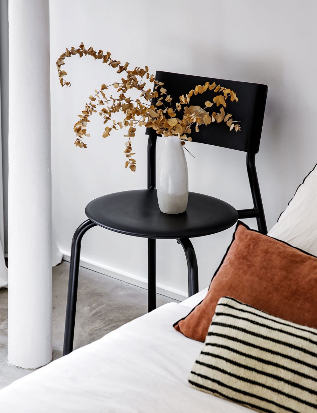 Minimalistische Einrichtung mit schwarzem Side-Table, weißer Vase und Kissen auf einem weißen Bett in elegantem Raum