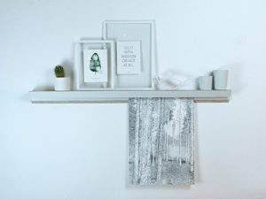 Minimalistisches Regal mit Bilderrahmen und Fotografie auf weißer Wand