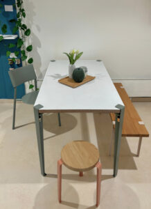 Ellie Tischplatte aus nachhaltigem Design, weißer Tisch mit Holzdecke, Vase und Kanne, umgeben von weißen Stühlen im
