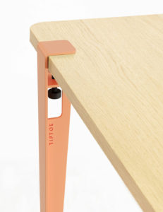 Minimalistische Tiptoe-Tischhalterung in Korallrosa auf hellen Holzplatte