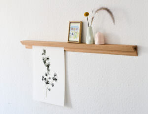 Holzregal mit Bilderrahmen und Blumen auf weißer Wand