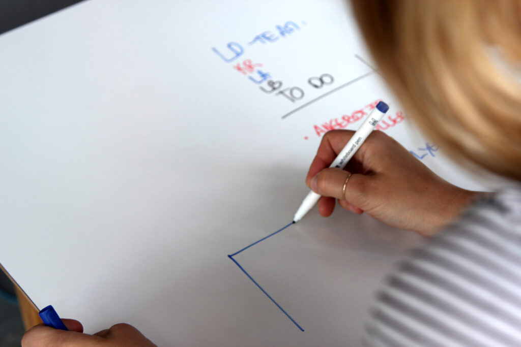 Frau an Whiteboard schreibt im Arbeitsraum zur Organisation und Planung