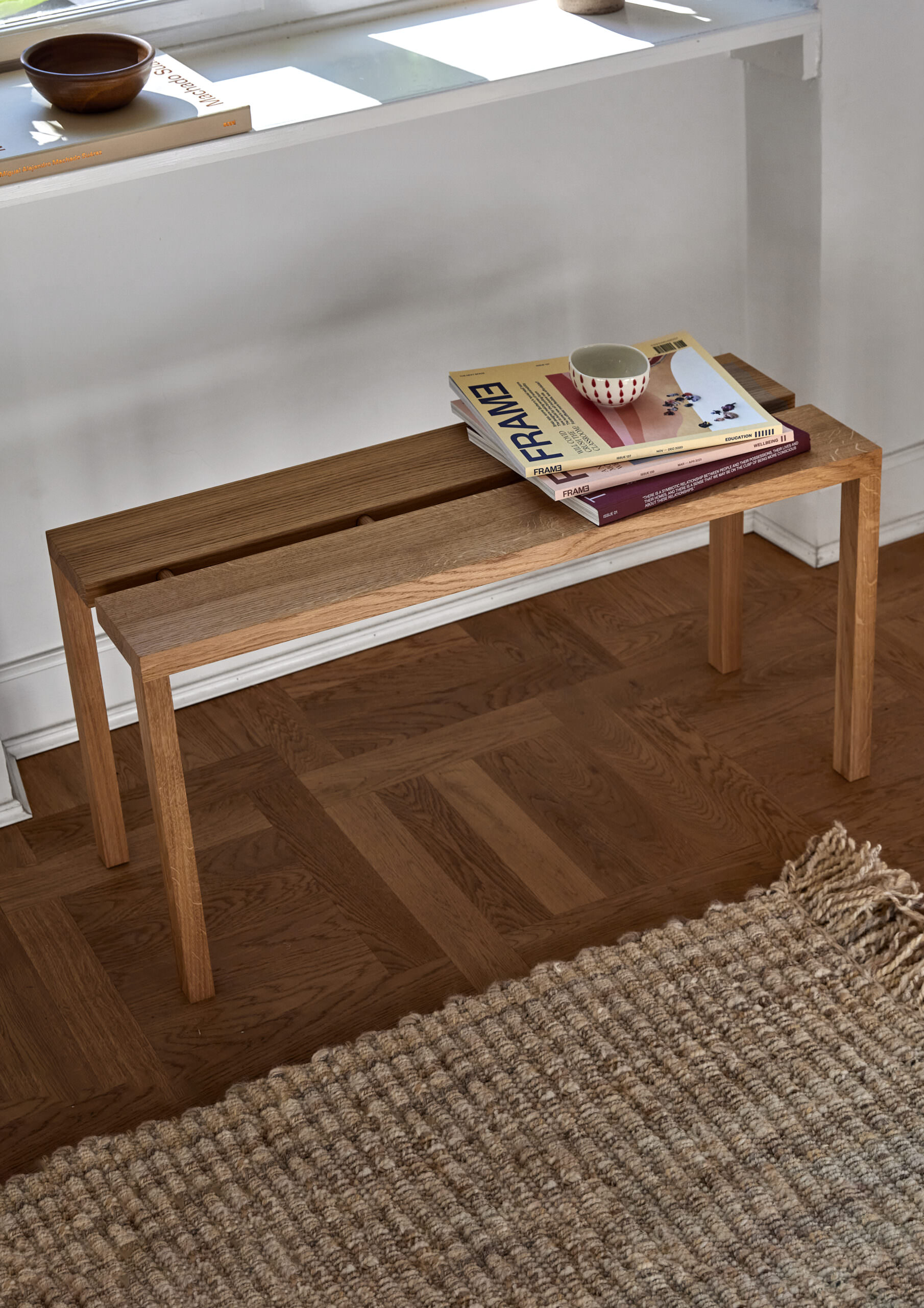 Minimalistische Holzbank aus hellem Eichenholz in warmer Braunfarbe auf weitem Parkettboden mit dezenten Accessoires