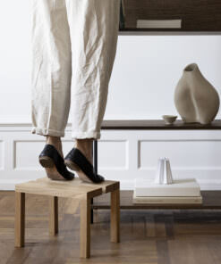 Weibliche Figur auf einem hölzernen Stuhl in einer gemütlichen Wohnumgebung mit Bücherregal und Vasen