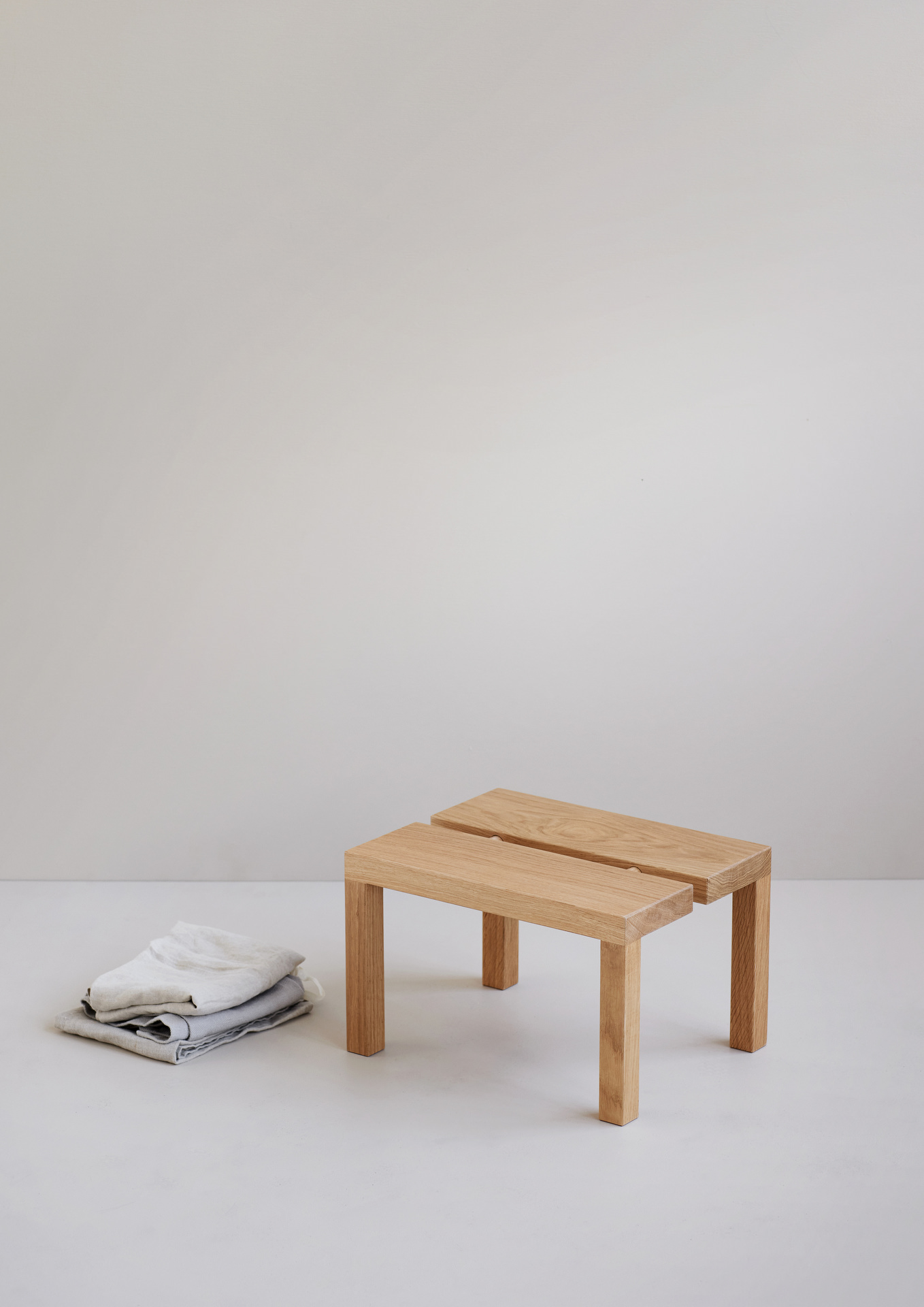 Holztisch mit klaren Formen und naturfarbigen Textilien auf weißem Hintergrund