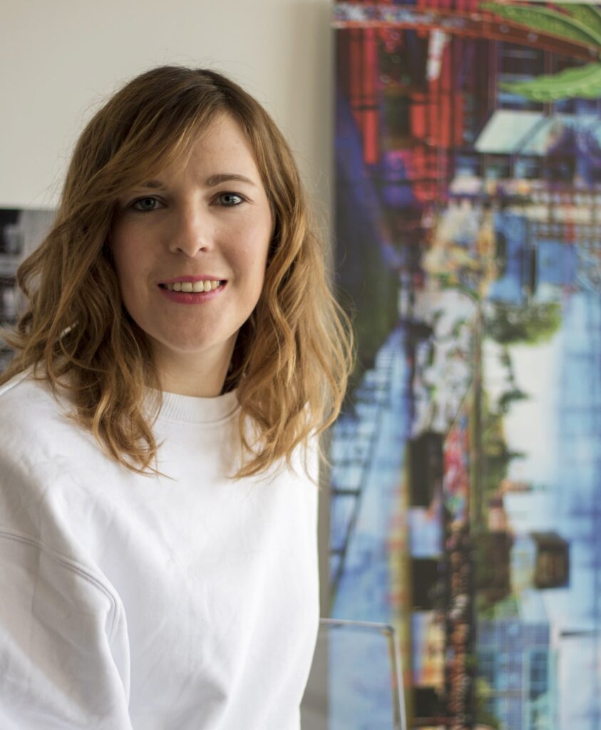 Lächelnde Designerin Annabelle Hoffmann vor farbenfroher Urban-Art-Wand im Hamburger Concept Store für nachhaltiges Design