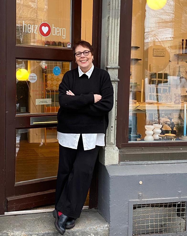 Frau vor offener weißer Tür, umgeben von nachhaltigen Designmöbeln, Wohnaccessoires und Interior im Hamburger Concept Store