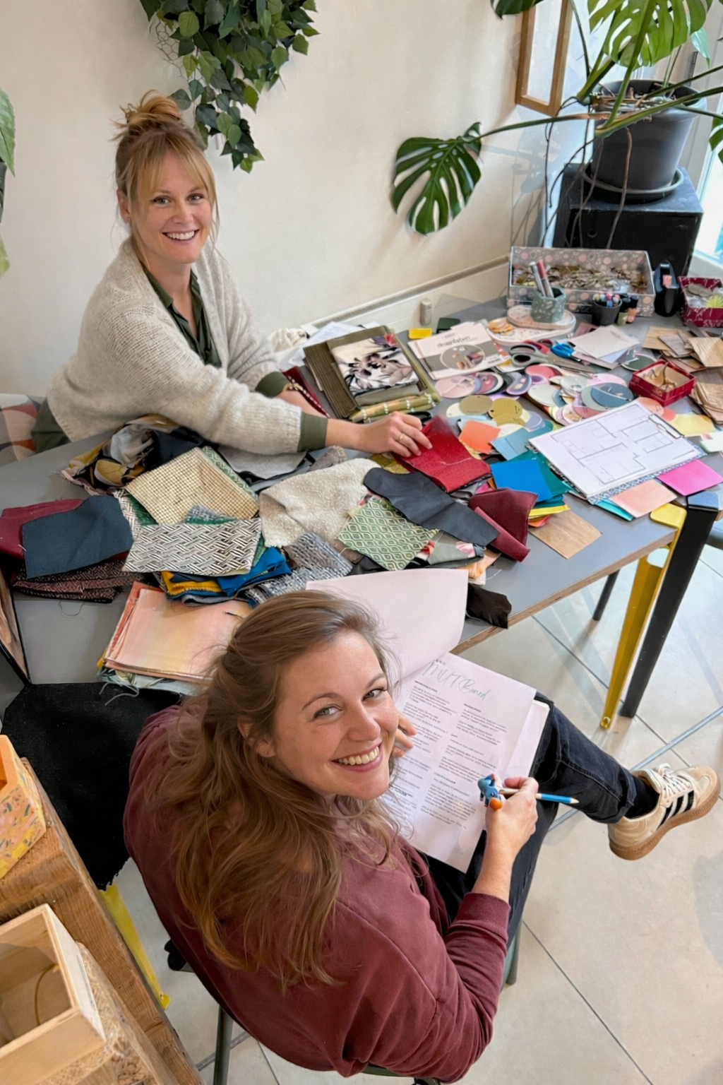 Zwei Frauen an einem Tisch mit Materialien, Büchern und Künstlervorräten in einer inspirierenden Arbeitsumgebung