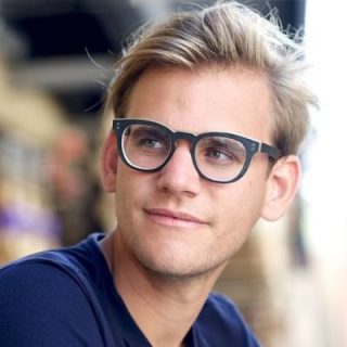 Mann mit Brille und blauem Hemd in einem Raum voller Möbel und Accessoires